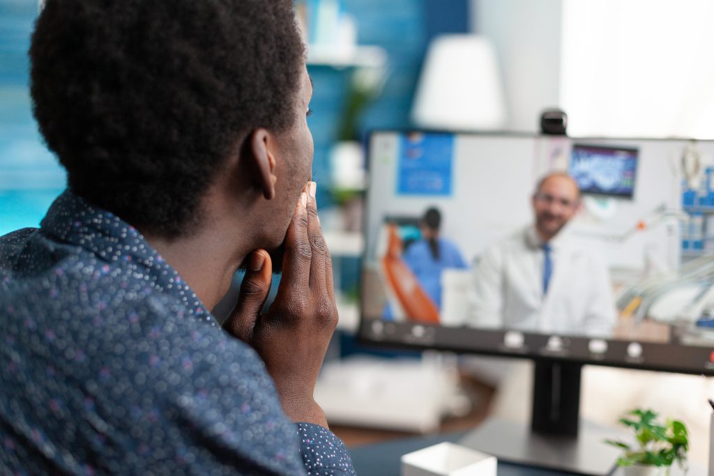 A person consults with a doctor via video call, holding their face while looking at the computer screen displaying the doctor, highlighting modern communication in healthcare.